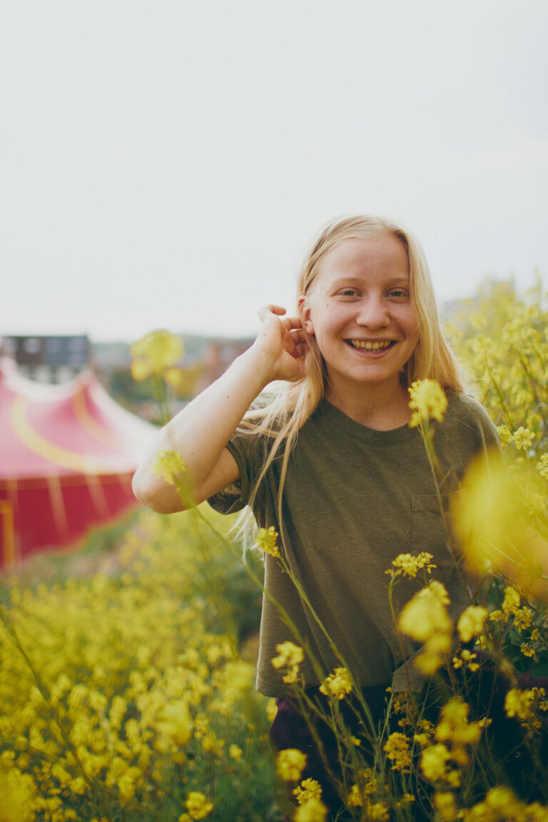 Saana Leppänen is standing in the middle of a field of blooming yellow flowers. The pink circus tent can be seen in the background.