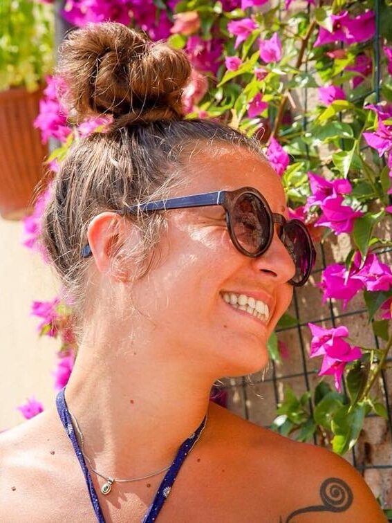 Irene wears some sunglasses while laughing in front of purple flowers in the background.